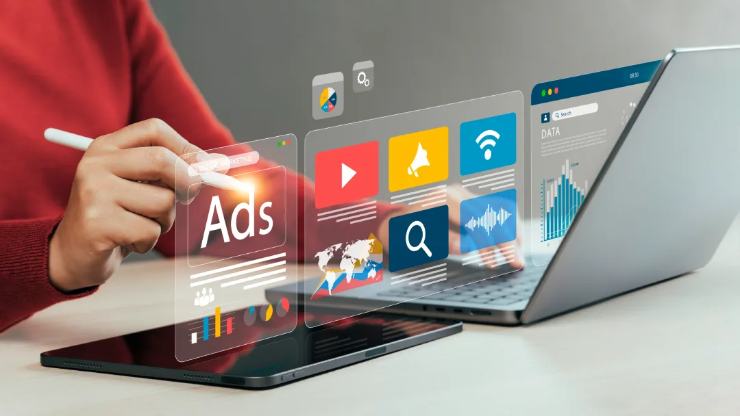 A marketer working across a laptop and tablet with digital advertising, search and analytics panels